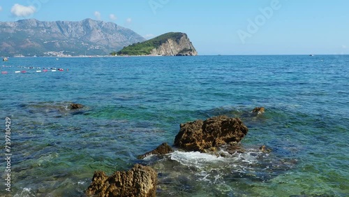 Budva, Montenegro. Beautiful summer day on the Adriatic Sea. Sveti Nikola island is located opposite to Old town of Budva. A cliff that rises 121 metres. Boats sail on water. Salty sea waves and rocks photo