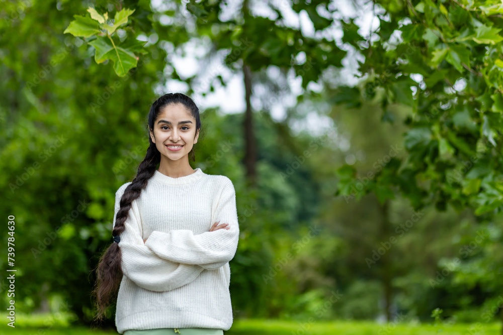Portrait of a smiling Indian young girl in a white sweater doing sports and walking in the park. He stands with his hands crossed on his chest and looks confidently into the camera Portrait of a smiling Indian young girl in a white sweater doing sports and walking in the park. He stands with his hands crossed on his chest and looks confidently into the camera