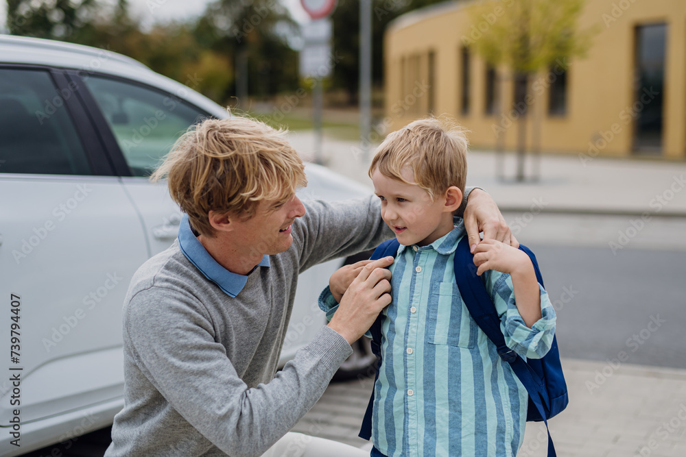 © Halfpoint - Father saying goodbyeto to son in front of school building, hugging him and helping with backpack. Dad heading to work. Concept of work-life balance for parents.