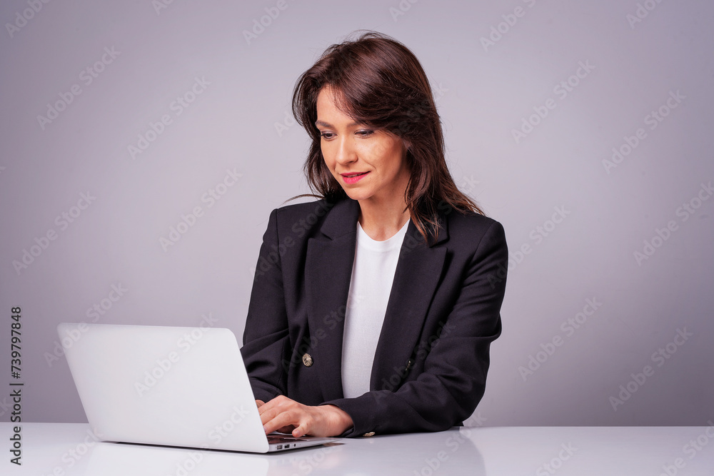 Studio shot of an attractive mid aged woman sitting at desk and using laptop against isolated white background Studio shot of an attractive mid aged woman sitting at desk and using laptop against isolated white background