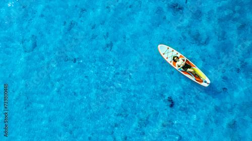 Aerial view of woman lying on a paddle board on the blue surface of the sea On holidays © Photo Sesaon