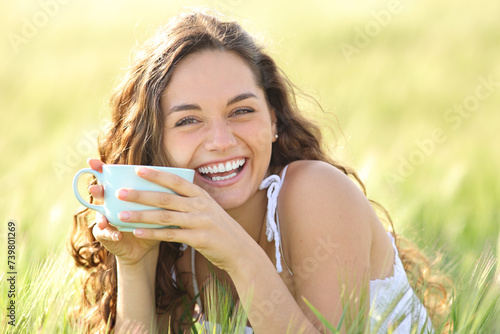 Happy woman laughing looking at you holding coffee cup in nature