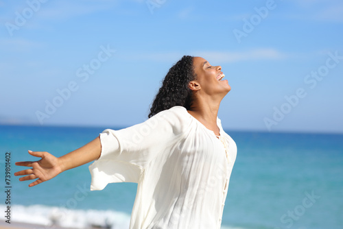 Happy black woman outstretching arms on the beach