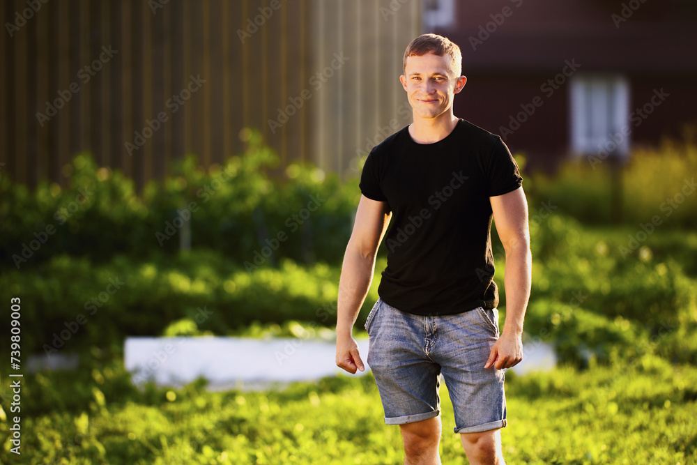 Horizontal knee length portrait of white man in her 20s, Caucasian male standing in garden at sunset
