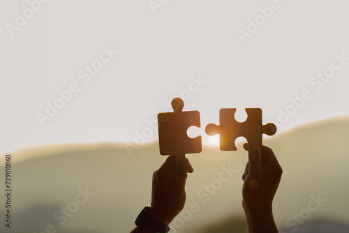 Silhouette Two hands of businessmen connecting a couple of puzzle pieces against the sunrise effect, partnership.Charity, Teamwork..Business solutions, targets, success, goals, and strategy concepts.