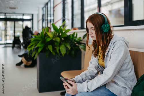 Teenage girl waiting in hospital corridor, listening music. Adolescent patient coming to hospital for examination. photo