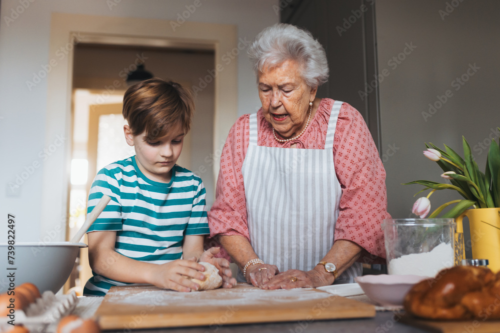 Grandmother with grandson preparing traditional easter meals, kneading dough for easter cross buns. Passing down family recipes, custom and stories.