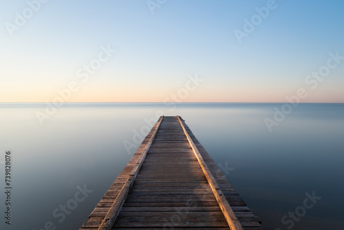 mystical photo of a rustic pier leading into a calm sea at sunrise