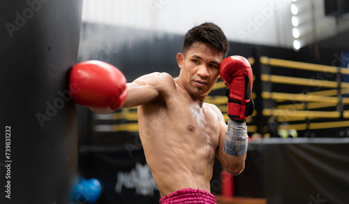 Male athlete boxing competition in ring. Asian ethnic man punch fighting in kickboxing exercise in fitness gym. Boxing is fighter sport training need body strength and power fist to knockout. © Nassorn
