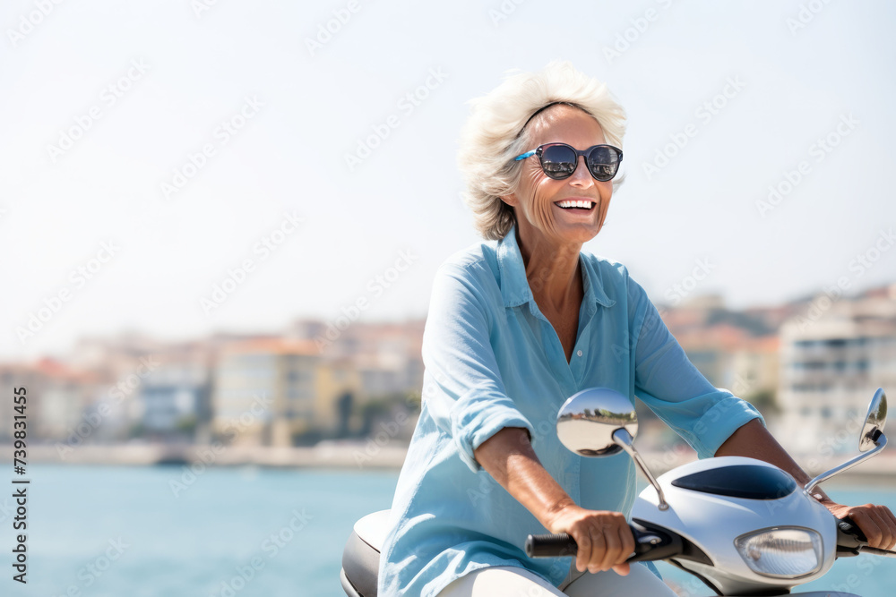 Joyful senior woman with sunglasses riding a scooter on a sunny day by the sea