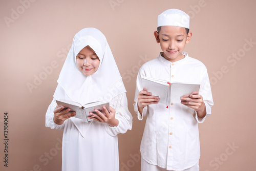 Little Asian muslim boy and girl wear cap and hijab reading Quran together