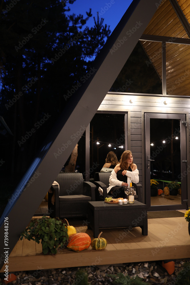 the girl drinks wine on the terrace of the house in the evening. autumn evening to sit on the terrace and drink wine in the evening. A-frame style house. romantic dinner on the terrace