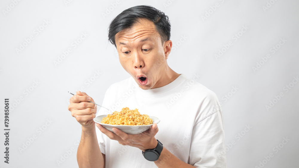 Portrait of an Indonesian Asian man, wearing a white T-shirt, enjoying eating noodles, isolated against a white background. Portrait of an Indonesian Asian man, wearing a white T-shirt, enjoying eating noodles, isolated against a white background.