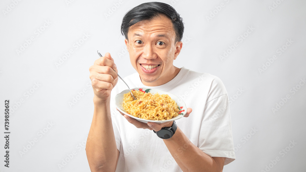 Portrait of an Indonesian Asian man, wearing a white T-shirt, enjoying eating noodles, isolated against a white background. Portrait of an Indonesian Asian man, wearing a white T-shirt, enjoying eating noodles, isolated against a white background.