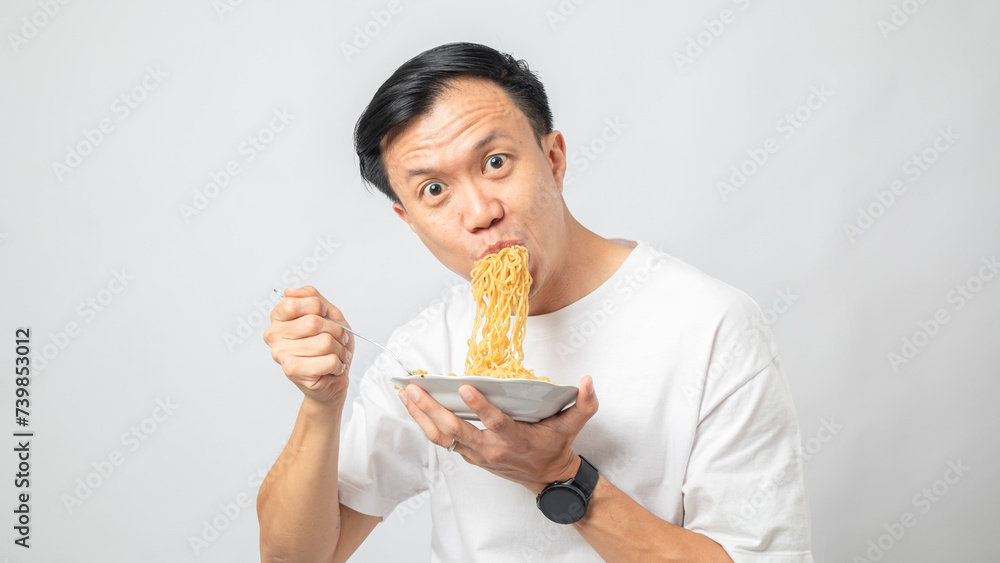 Portrait of an Indonesian Asian man, wearing a white T-shirt, enjoying eating noodles, isolated against a white background. Portrait of an Indonesian Asian man, wearing a white T-shirt, enjoying eating noodles, isolated against a white background.