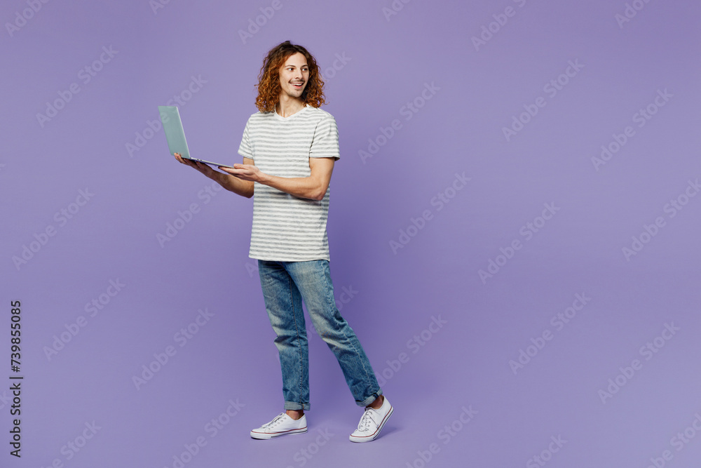 Fototapeta premium Full body smart fun young IT man he wears grey striped t-shirt casual clothes hold use work on laptop pc computer isolated on plain pastel light purple background studio portrait. Lifestyle concept.