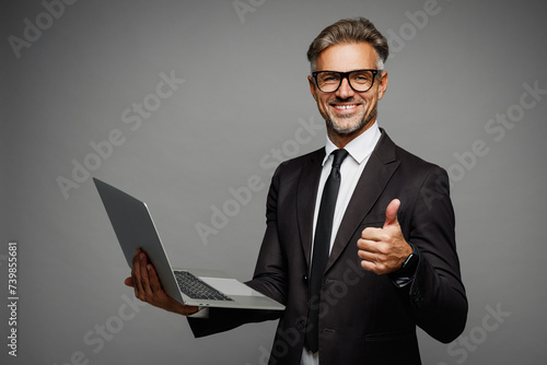 Side view happy adult employee IT business man corporate lawyer he wears classic formal black suit shirt tie work in office hold use laptop pc computer show thumb up isolated on plain grey background. photo