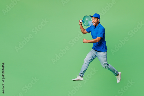 Full body fun delivery guy employee man wear blue cap t-shirt uniform workwear work as dealer courier hold big large clear water bottle jump high isolated on plain green background. Service concept.