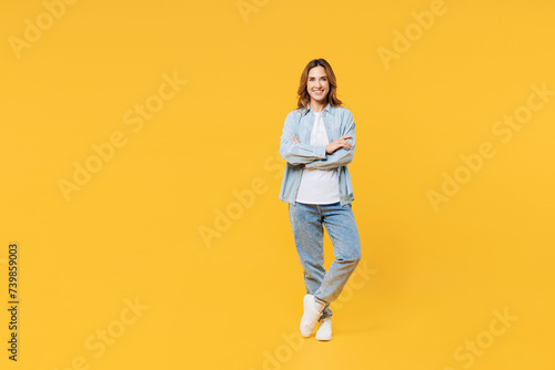 Full body smiling happy cool young woman she wear blue shirt white t-shirt casual clothes hold hands crossed folded look camera isolated on plain yellow background studio portrait. Lifestyle concept.