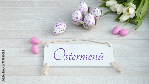 Der Text Ostermenü auf ein Schild geschrieben mit Osterdekoration und Blumen.