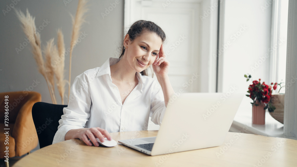 Smiling woman working on laptop in a bright room with flowers, epitomizing remote work and cozy home office. Smiling woman working on laptop in a bright room with flowers, epitomizing remote work and cozy home office.