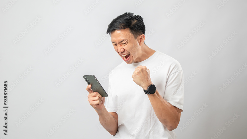 Portrait of an Indonesian Asian man, wearing a white T-shirt, looking expressive at his smartphone, isolated against a white background. Portrait of an Indonesian Asian man, wearing a white T-shirt, looking expressive at his smartphone, isolated against a white background.