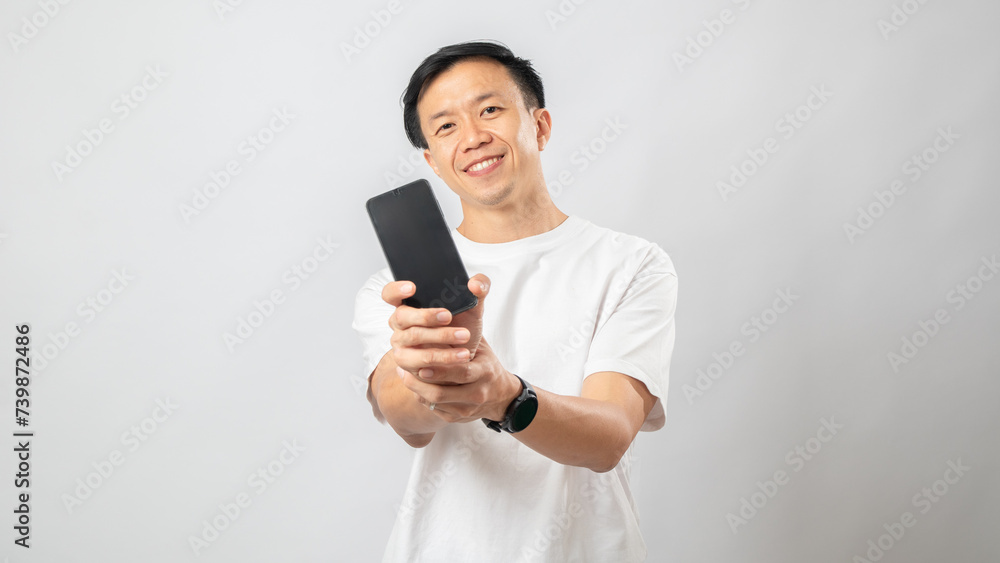 Portrait of an Indonesian Asian man, wearing a white T-shirt, showing the blank screen of his smartphone, isolated against a white background. Portrait of an Indonesian Asian man, wearing a white T-shirt, showing the blank screen of his smartphone, isolated against a white background.