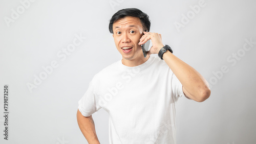 Portrait of an Indonesian Asian man, wearing a white T-shirt, talking on his smartphone, isolated against a white background.