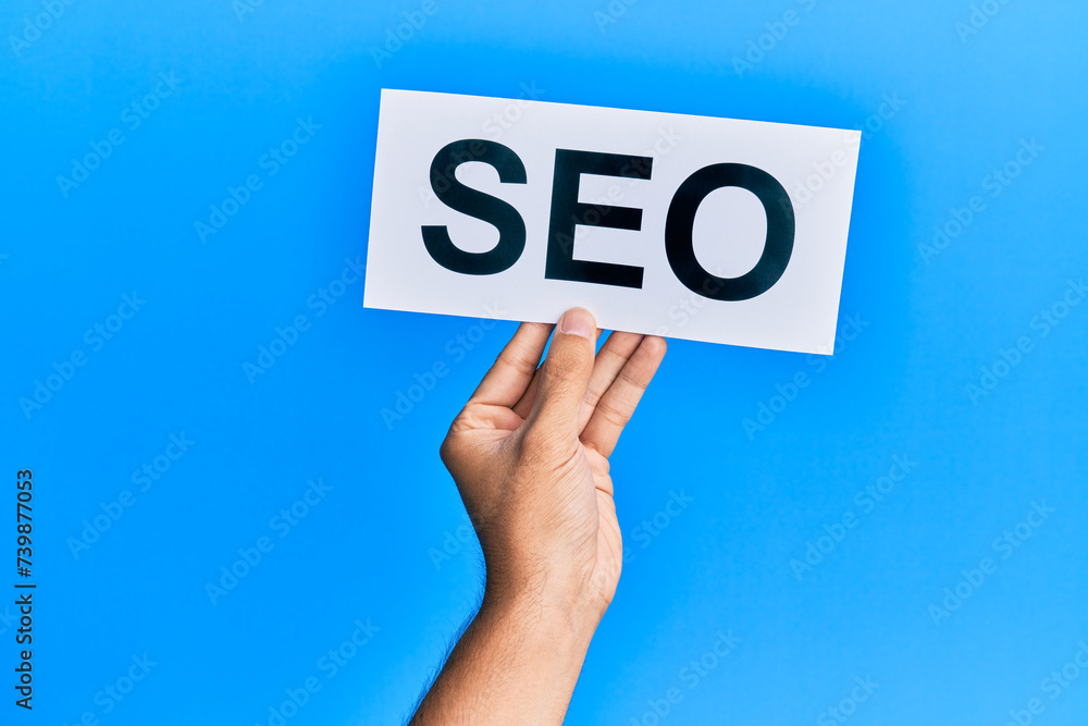 Hand of caucasian man holding paper with seo word over isolated blue background Hand of caucasian man holding paper with seo word over isolated blue background