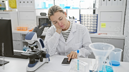 A focused woman scientist in a laboratory using a smartphone while working next to a microscope and test tubes.