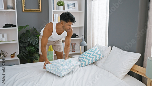 A young hispanic man arranges pillows in a modern bedroom at home, showcasing a tidy and stylish interior. photo