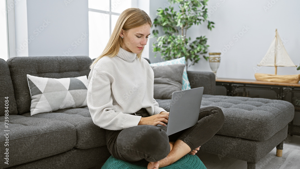 A blonde woman works on her laptop while seated comfortably in a modern living room, exuding casual elegance A blonde woman works on her laptop while seated comfortably in a modern living room, exuding casual elegance