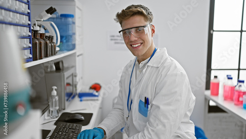Handsome  confident young caucasian man  a smiling scientist  dives into medical research on his computer in the bustling  high-tech lab  his fingers happily typing away.