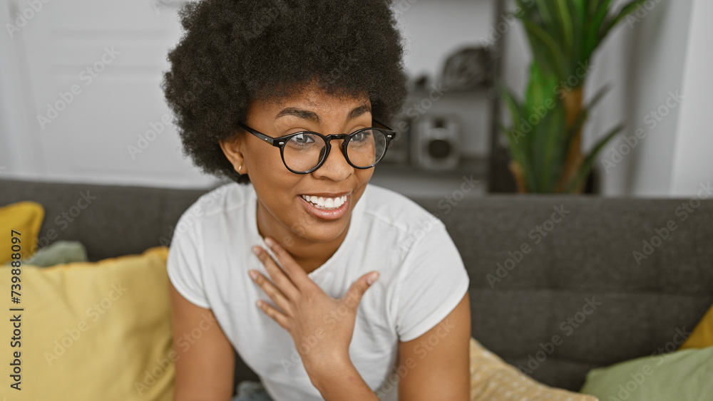 Smiling african american woman with glasses sitting indoors on her sofa surrounded by cushions Smiling african american woman with glasses sitting indoors on her sofa surrounded by cushions
