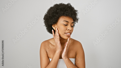 A beautiful african american woman with curly hair poses elegantly against a white background, touching her face gently.