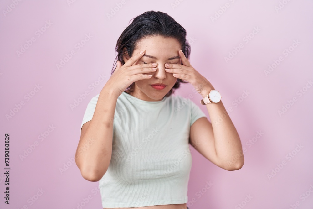 Hispanic young woman standing over pink background rubbing eyes for fatigue and headache, sleepy and tired expression. vision problem Hispanic young woman standing over pink background rubbing eyes for fatigue and headache, sleepy and tired expression. vision problem