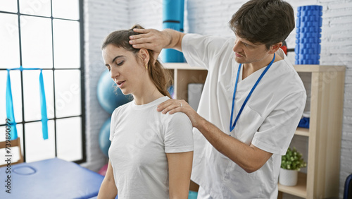 A physiotherapist man treats a woman patient in a white rehab room with blue mats.