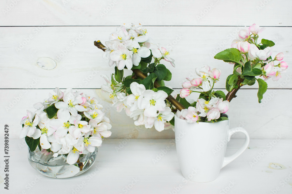 A beautiful sprig of an apple tree with white flowers in a cap against a white wooden background. Blossoming branch in a glass with water. Spring still life. Concept of spring or mom day A beautiful sprig of an apple tree with white flowers in a cap against a white wooden background. Blossoming branch in a glass with water. Spring still life. Concept of spring or mom day