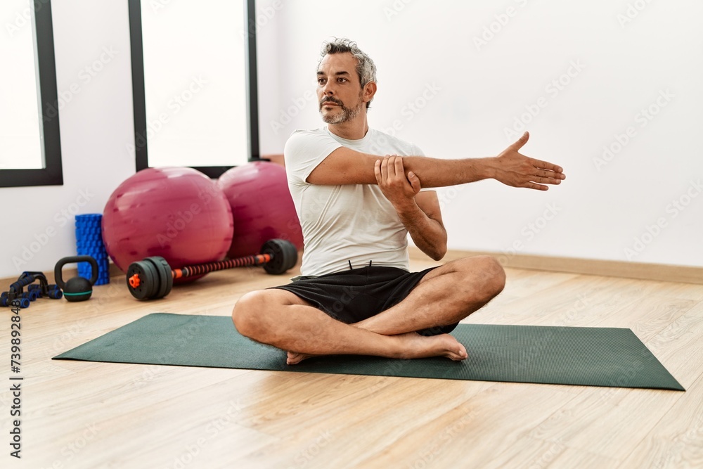 Fototapeta premium Middle age grey-haired man stretching arm at sport center