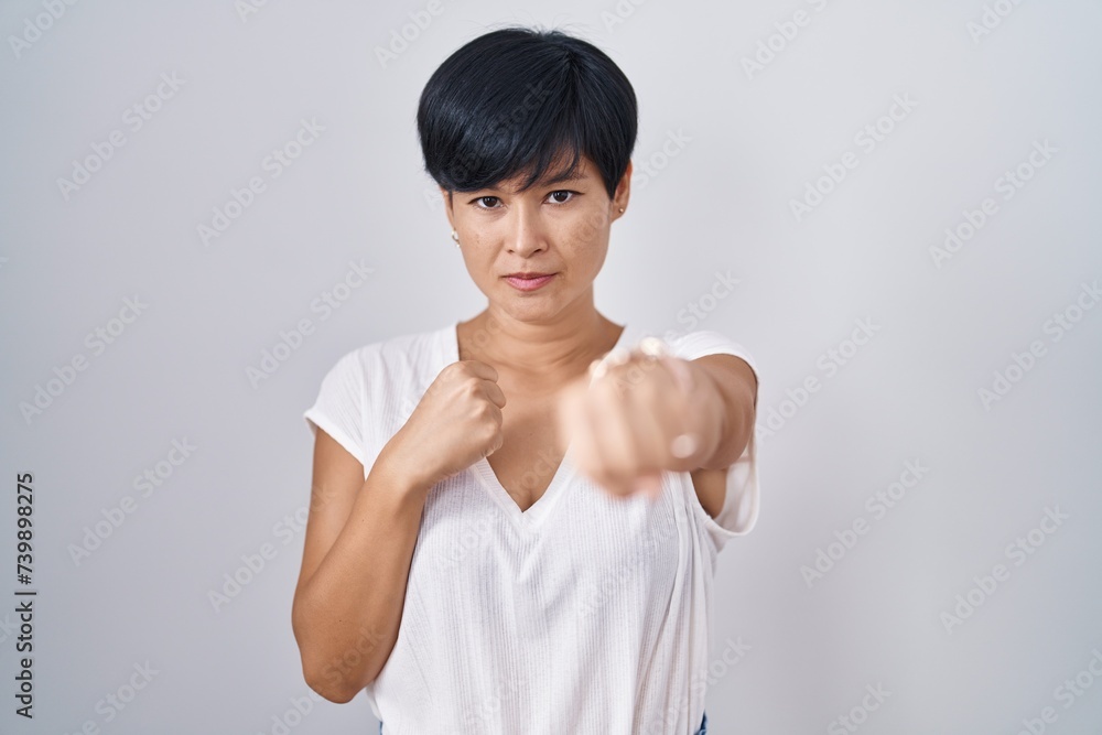 Young asian woman with short hair standing over isolated background punching fist to fight, aggressive and angry attack, threat and violence Young asian woman with short hair standing over isolated background punching fist to fight, aggressive and angry attack, threat and violence