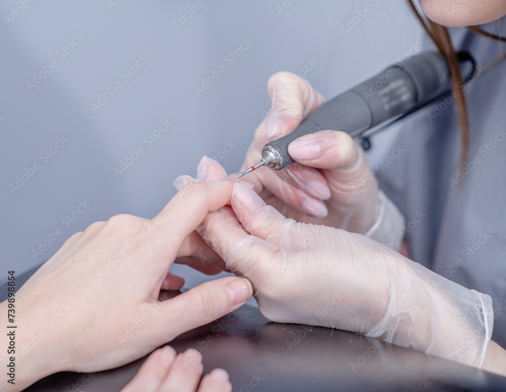 Close up professional manicure master using electric machine in beauty salon to remove nail polish hands during manicure procedure Close up professional manicure master using electric machine in beauty salon to remove nail polish hands during manicure procedure