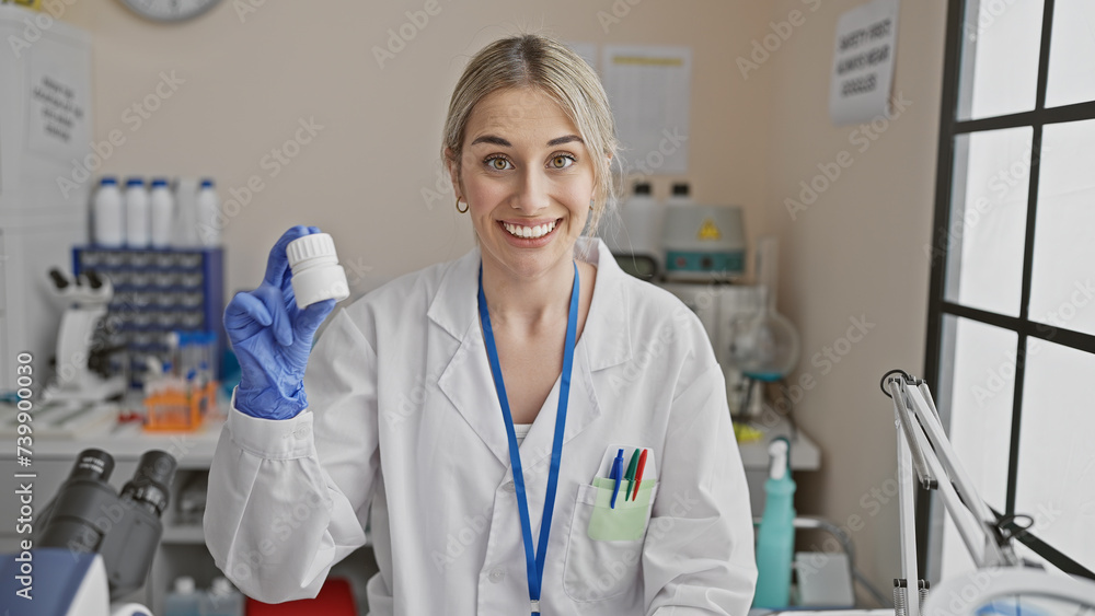 A cheerful young woman in a lab coat holding a medicine bottle in a bright laboratory setting.