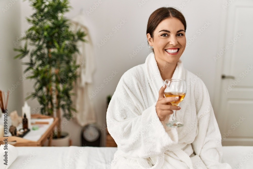 Young beautiful hispanic woman wearing bathrobe drinking wine at beauty salon Young beautiful hispanic woman wearing bathrobe drinking wine at beauty salon