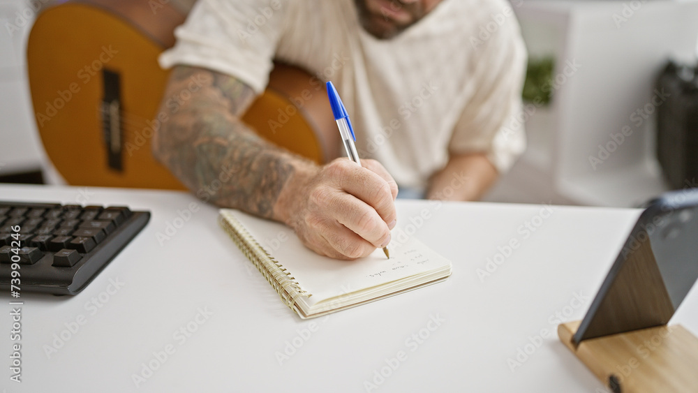 Handsome young man, relaxed & concentrating, composing classic music, playing acoustic guitar in cozy music studio Handsome young man, relaxed & concentrating, composing classic music, playing acoustic guitar in cozy music studio