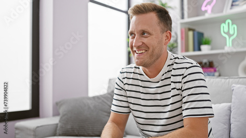 Confident young caucasian man happily resting on his cozy sofa, enjoying the comfort of home with a relaxing smile