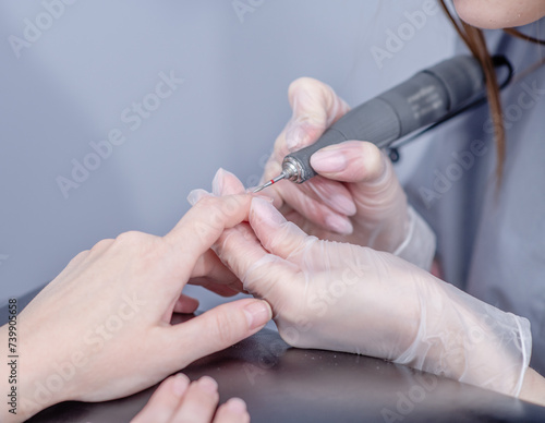 Close up professional manicure master using electric machine in beauty salon  to remove nail polish hands during manicure procedure