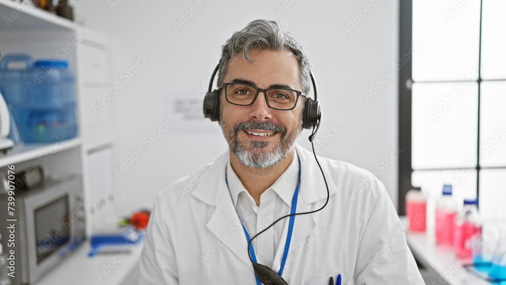 Young hispanic grey-haired man scientist wearing headphones having video call at laboratory Young hispanic grey-haired man scientist wearing headphones having video call at laboratory