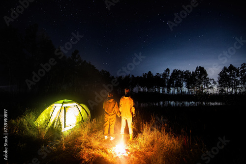 A couple of tourists standing at bonfire in their camp and looking to night sky