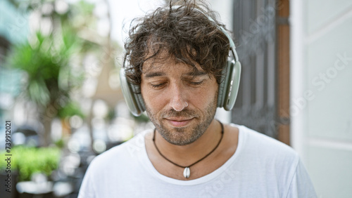 A handsome young man listening to music with headphones on an urban city street, exuding a relaxed vibe.