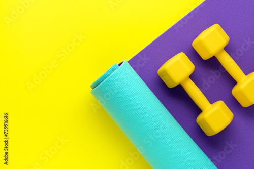 Dumbbells for sports on roll mat, yellow background. Top view, copy space. Bodybuilding workout concept. Flat lay. Fitness equipment. Mock up. Athletic training.